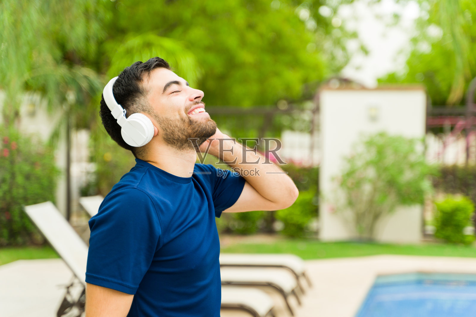 在泳池边锻炼后，戴着耳机享受音乐的健康年轻人微笑着照片摄影图片