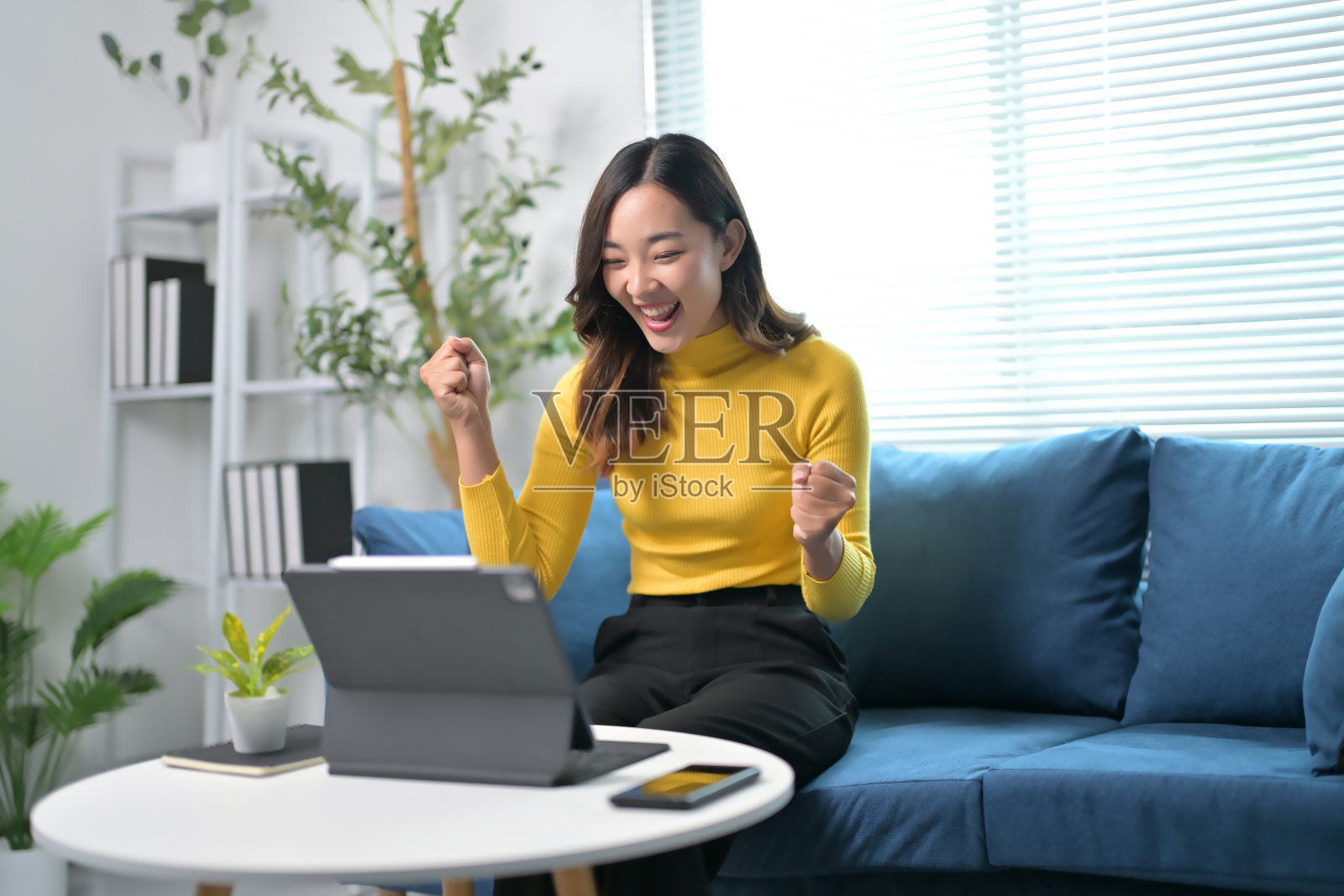 在现代家庭办公环境中，兴奋的女性在平板电脑上庆祝成功照片摄影图片