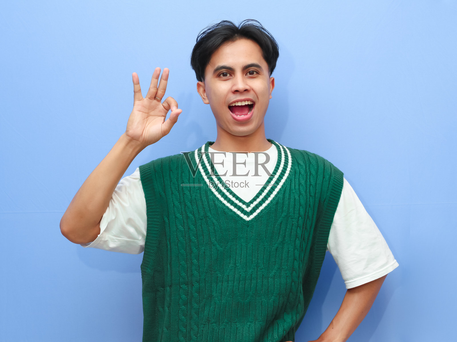 我很好。开心兴奋的亚洲人的肖像，用手指做认可的手势，微笑，表明他很好，孤立在蓝色的工作室背景。自信积极的青少年很酷照片摄影图片