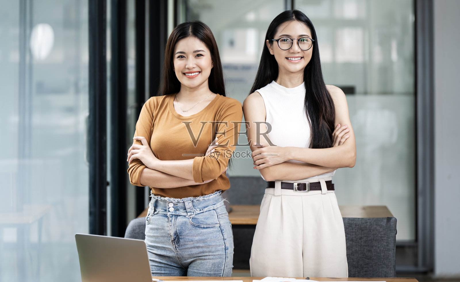 两位微笑自信的女士双臂交叉站在办公室的肖像。女性力量伙伴关系。照片摄影图片