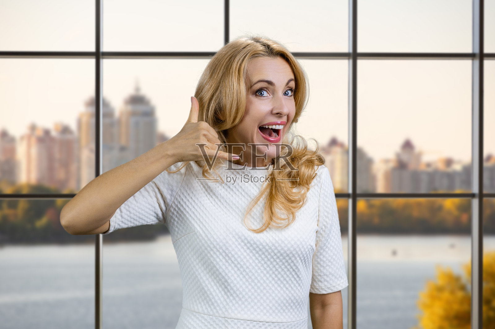 快乐成熟的金发女商人表演叫我手势。照片摄影图片