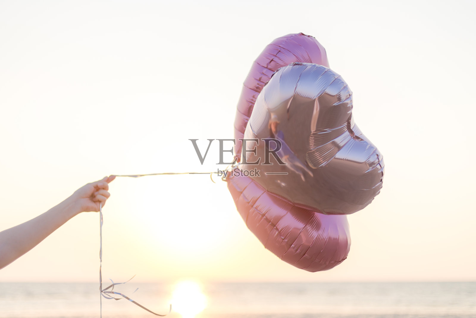 在晴朗的天空下，沙滩上手持气球的女子的手被剪短了照片摄影图片