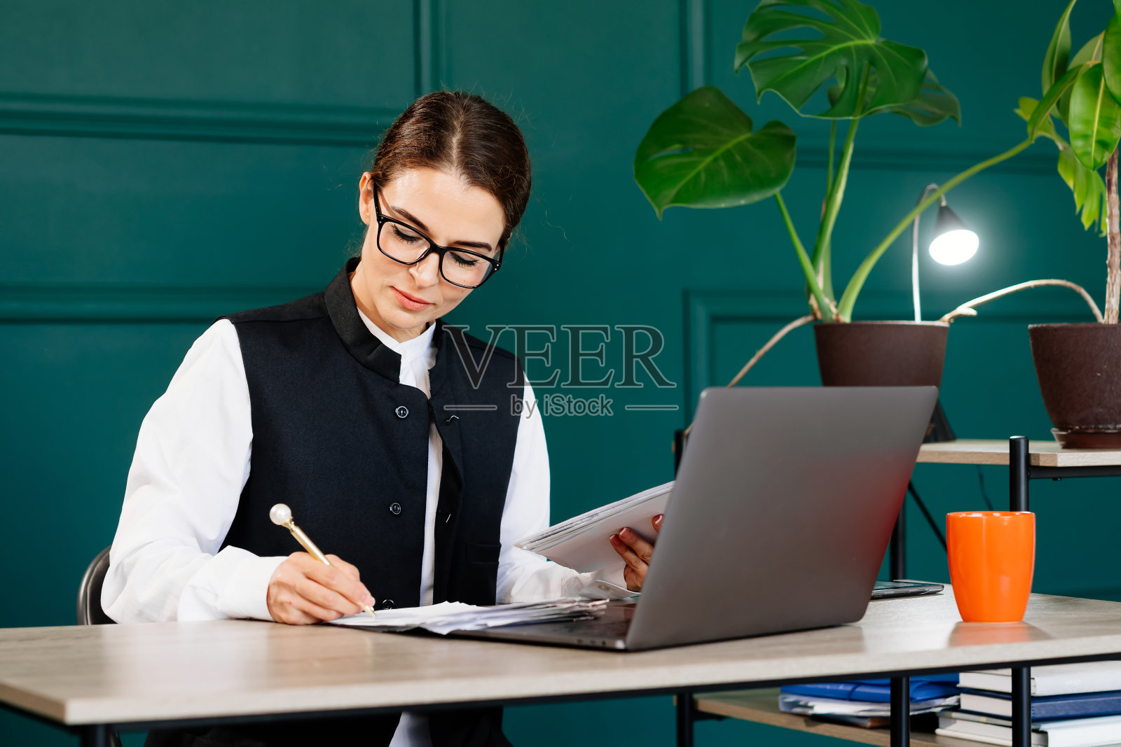 时髦的年轻女子在现代办公室里用笔记本电脑工作。非常适合生产力，商业和现代工作环境的概念。照片摄影图片