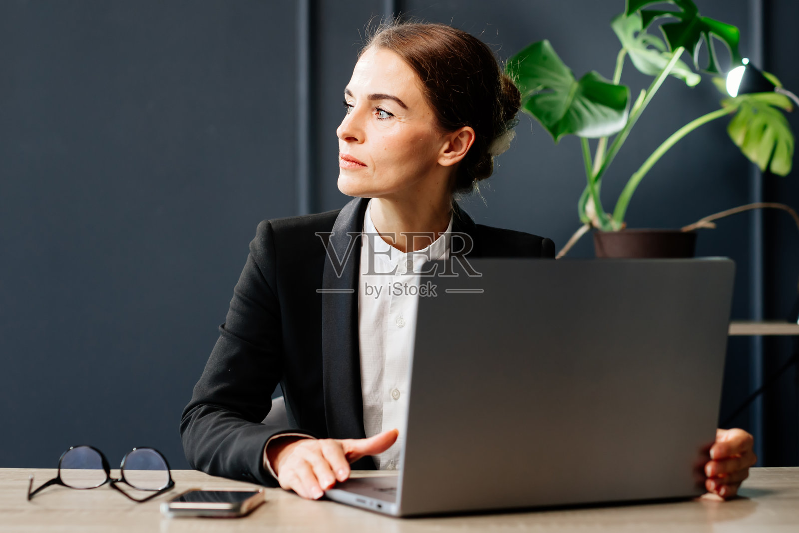 时髦的年轻女子在现代办公室里用笔记本电脑工作。非常适合生产力，商业和现代工作环境的概念。照片摄影图片