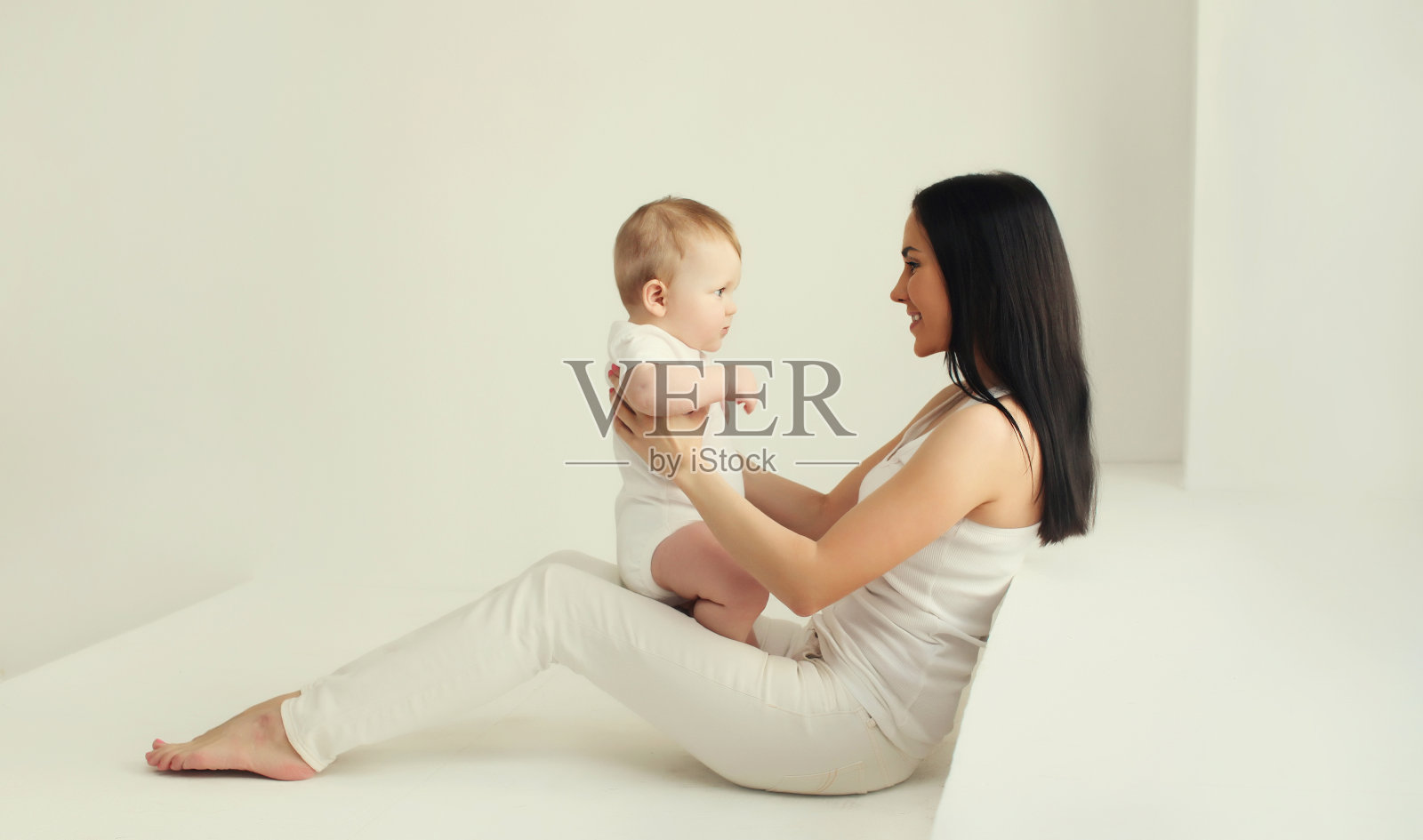 快乐微笑的年轻妈妈在家里的白色房间里和宝宝玩耍照片摄影图片