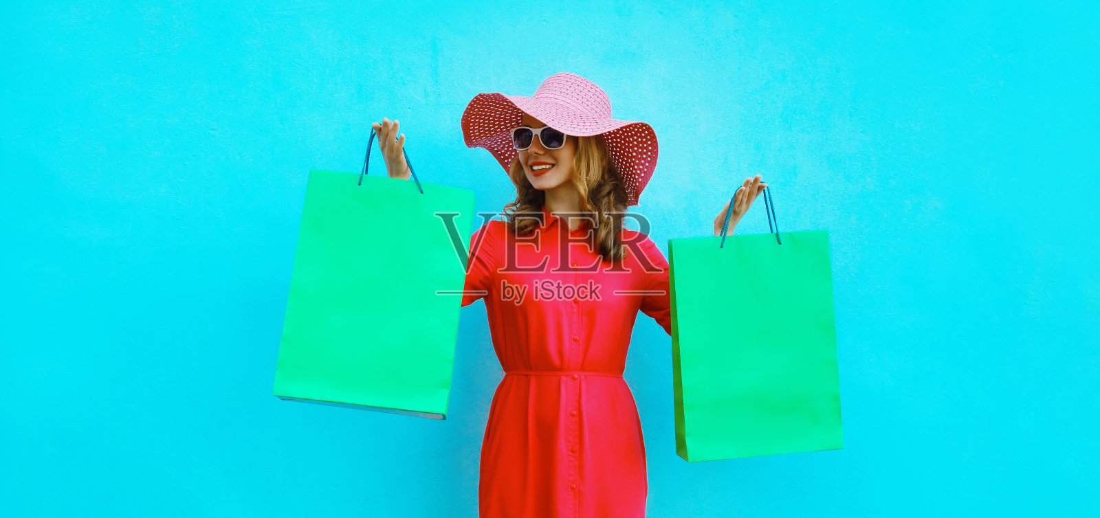 优雅、美丽、快乐的年轻女性模特穿着粉红色的连衣裙，戴着夏日帽，拿着购物袋摆姿势照片摄影图片