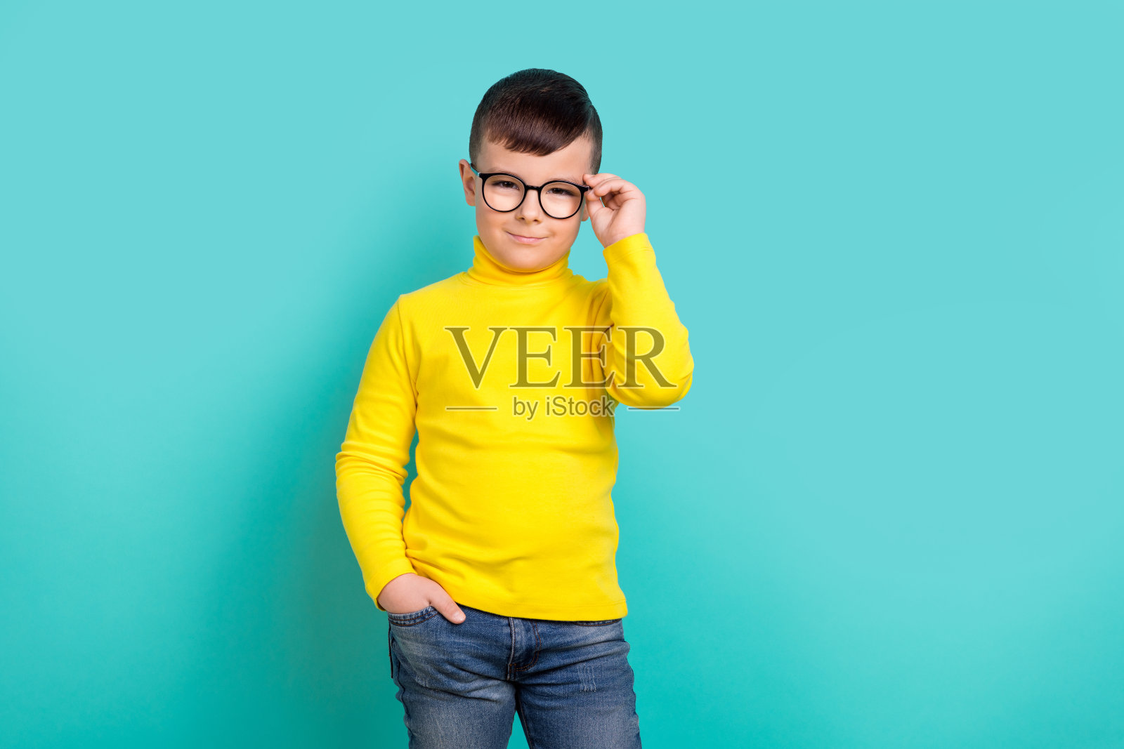 照片中的聪明男孩一年级学生小天才触摸眼镜孤立的青色背景照片摄影图片