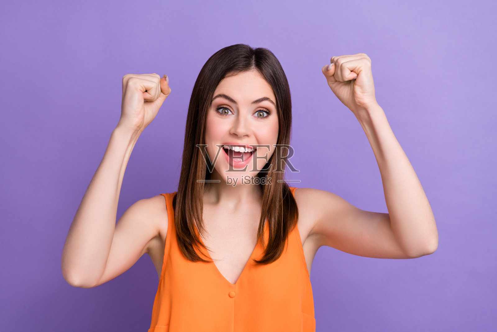 在紫色的背景上，可爱的女孩咧嘴笑着举起拳头喊着“是的，万岁”照片摄影图片
