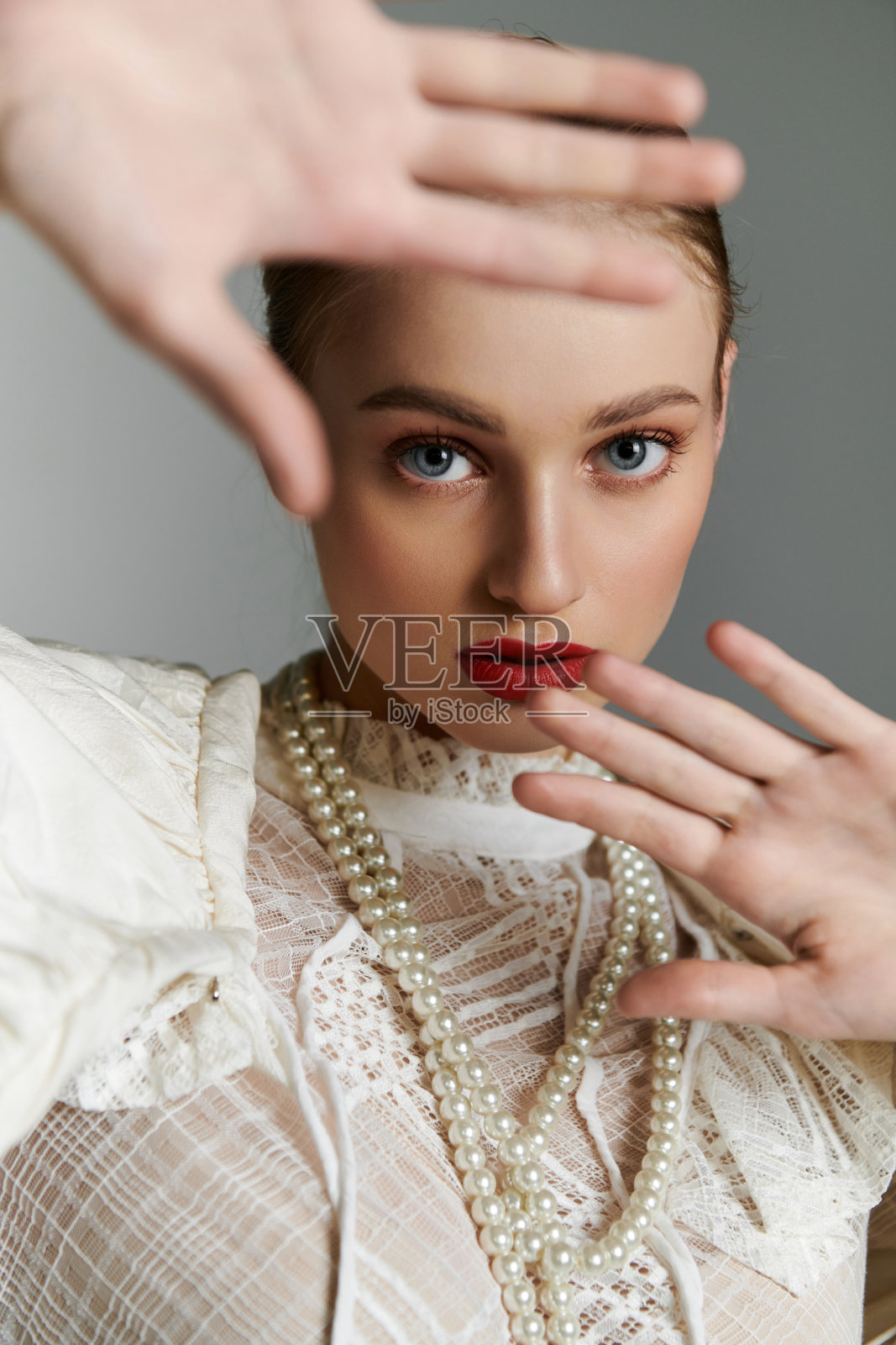 年轻女子摆姿势拍照，双手放在脸前，露出珍珠项链和红色唇膏。照片摄影图片