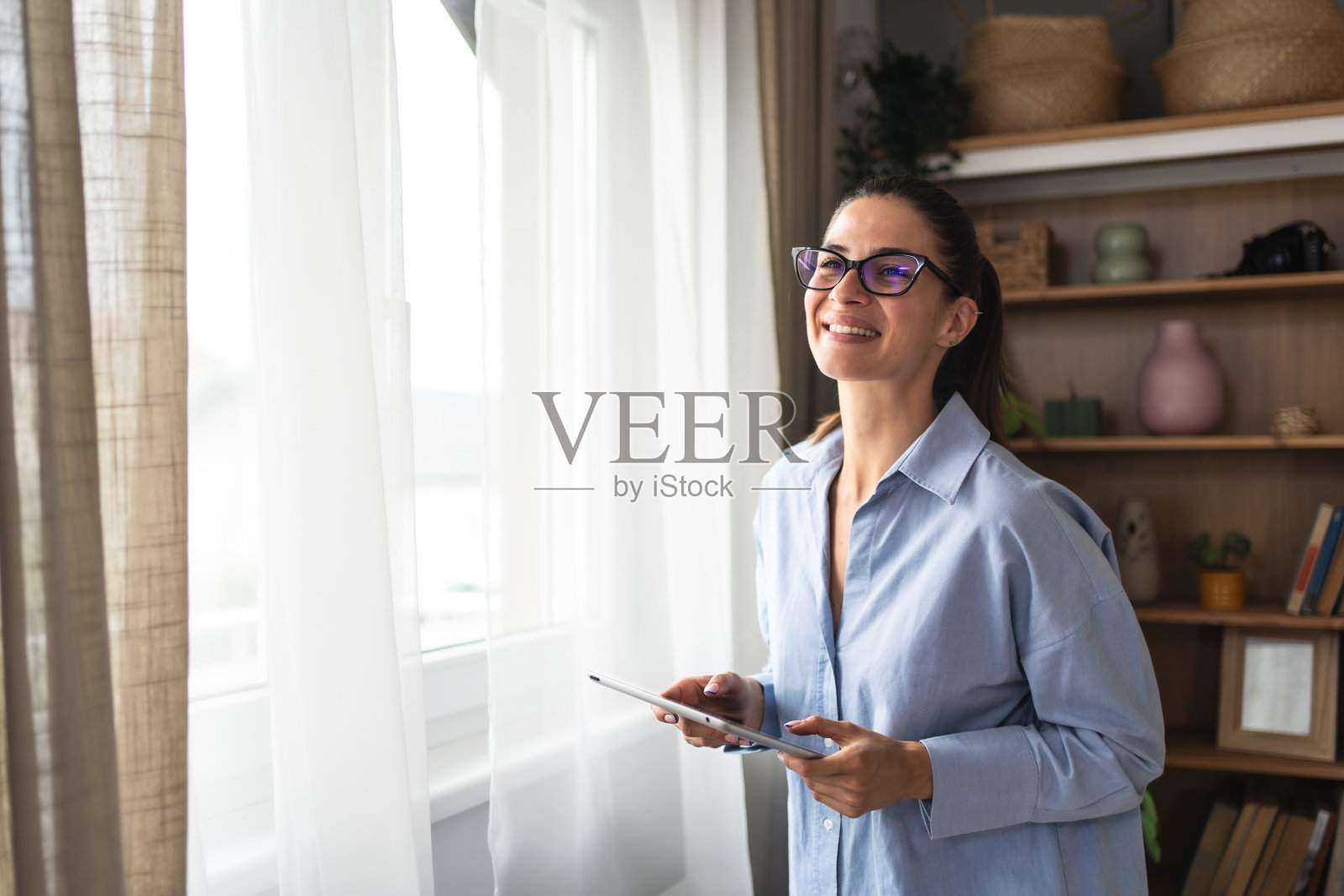 房地产经纪人用平板电脑向窗外看。年轻的女商人在家工作，使用电子设备。成功的专业职业平面设计师女性在工作之余休息。照片摄影图片