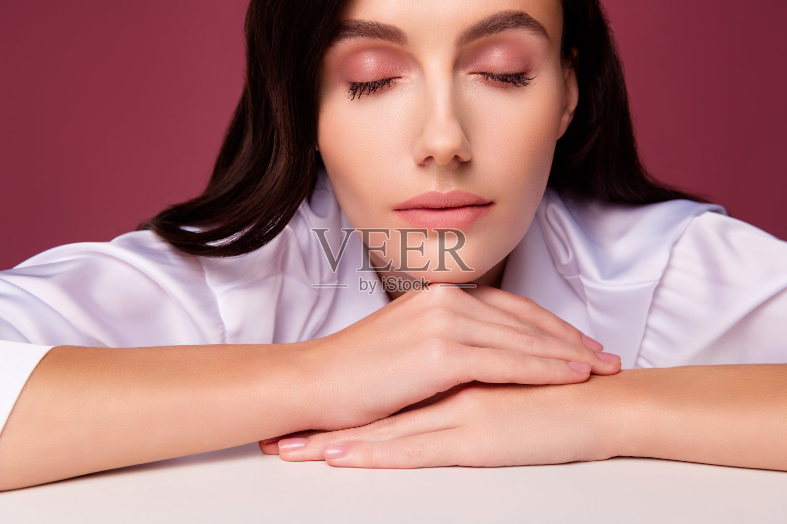 女孩闭着眼睛看着相机的特写照片，手儿子桌子孤立的粉红色背景照片摄影图片