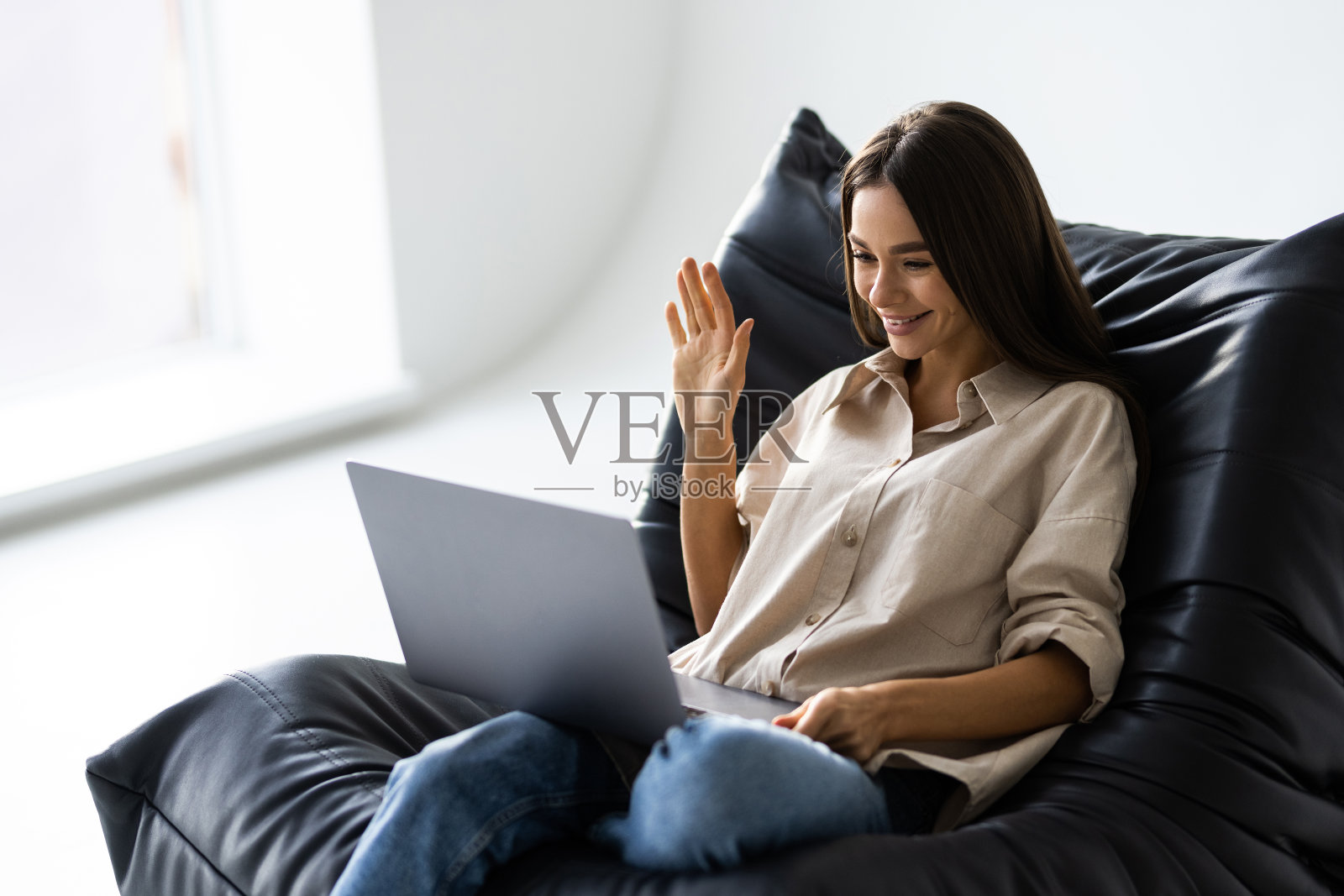 放松的年轻女子坐在包椅上，伸展着手臂，用着笔记本电脑照片摄影图片