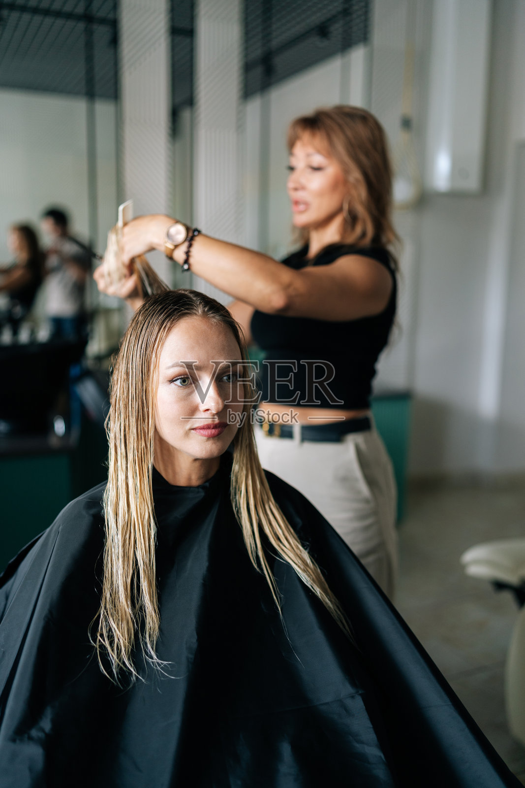 女理发师用专业的剪刀为年轻的金发女客户做时尚的发型。照片摄影图片