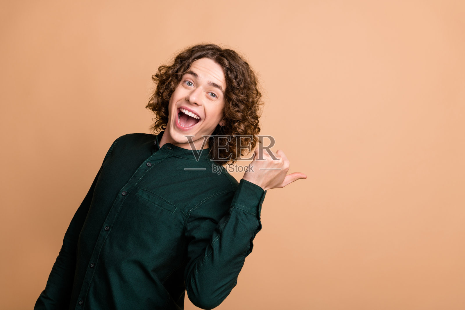 年轻的酷时髦的开朗有趣的男人穿着绿色时髦的衣服，在米色的背景上呈现出空白的空间照片摄影图片