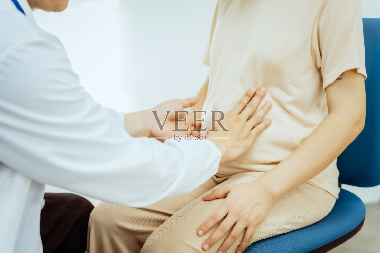 一位穿白大褂的亚洲儿科男医生坐在办公桌前，热情地迎接一位中年孕妇进行产前咨询，在临床环境中提供护理和支持照片摄影图片