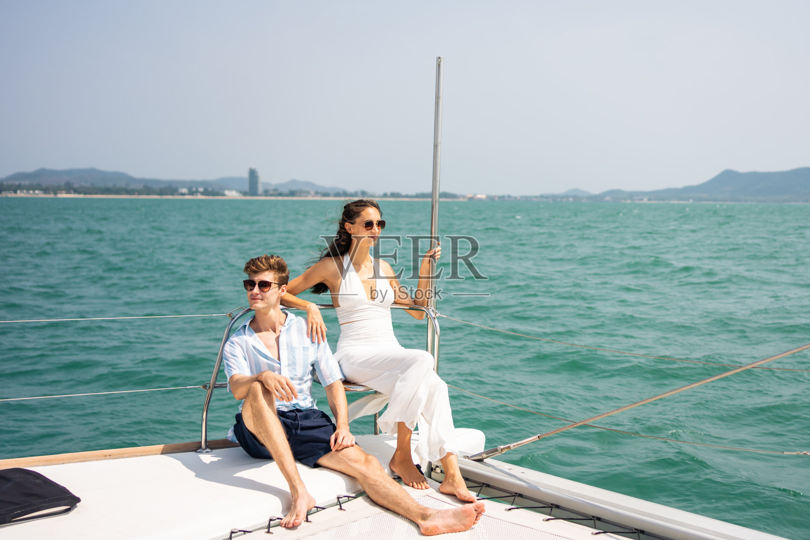 一对浪漫的高加索夫妇在游艇上欣赏美丽的景色。迷人的年轻男女在夏日夕阳下的双体船中一起庆祝蜜月旅行照片摄影图片