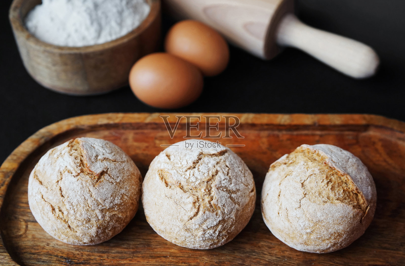 小的新鲜面包放在木托盘上，旁边是鸡蛋、面粉和擀面杖照片摄影图片