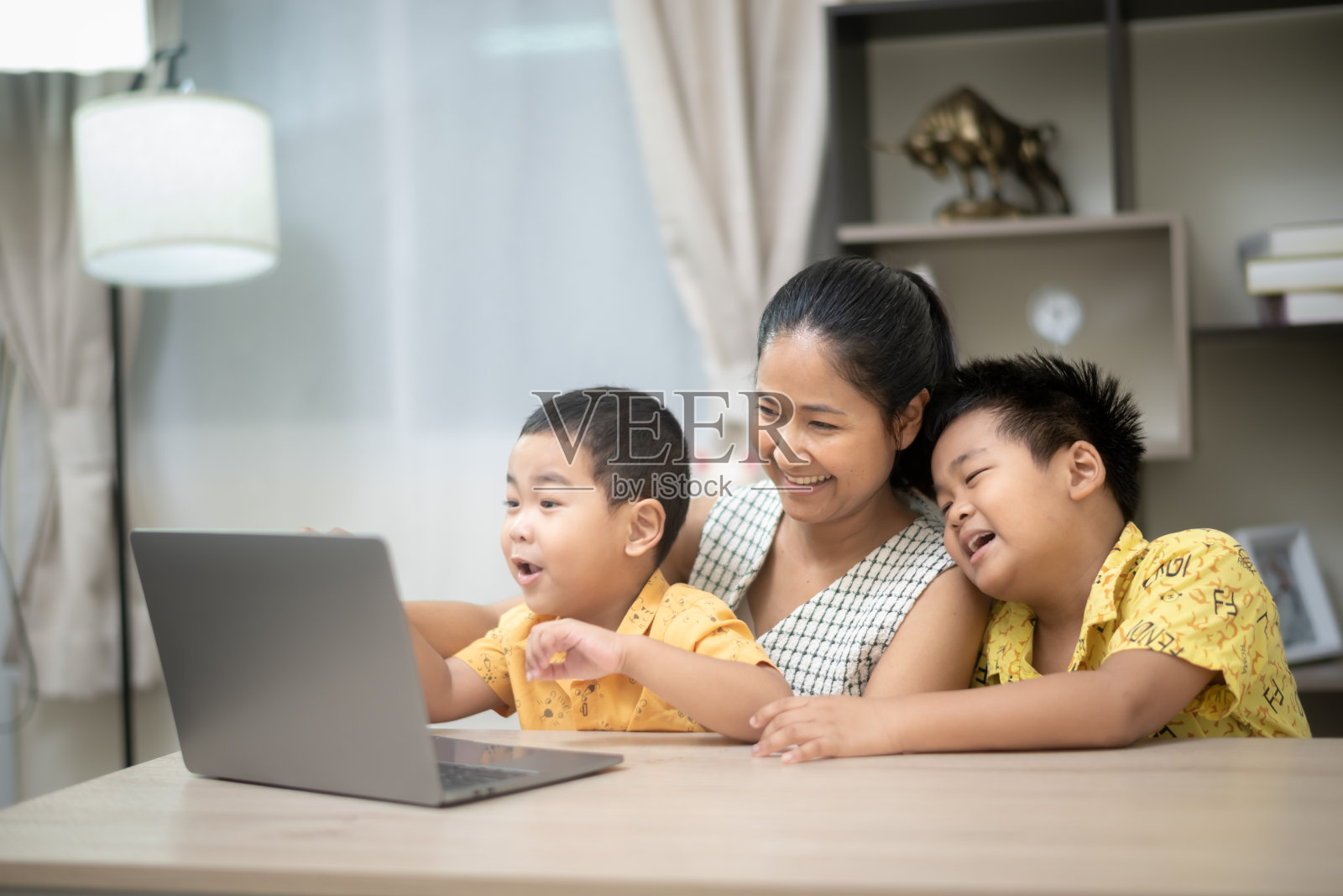 一位母亲和她的两个年幼的儿子在明亮、舒适的家庭环境中愉快地玩着笔记本电脑，一起探索科技。照片摄影图片