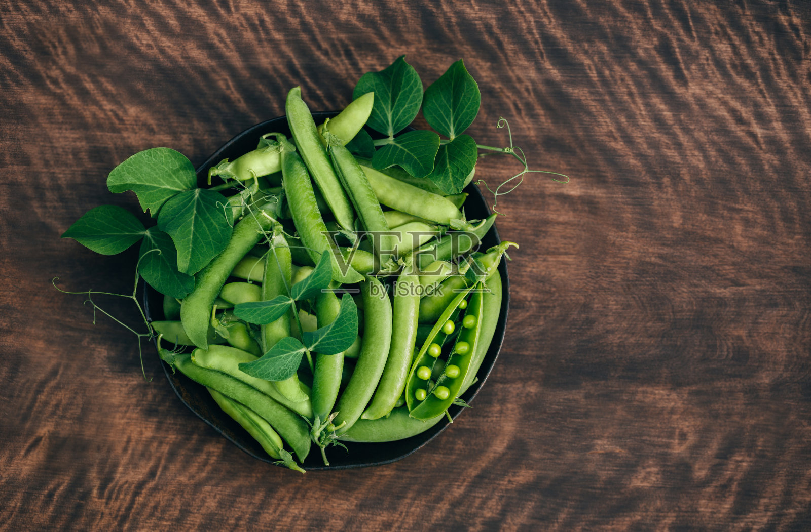 有豆荚和叶子的绿色豌豆放在一个碗里，木质背景上有复制空间。有机蔬菜。从上面看。照片摄影图片