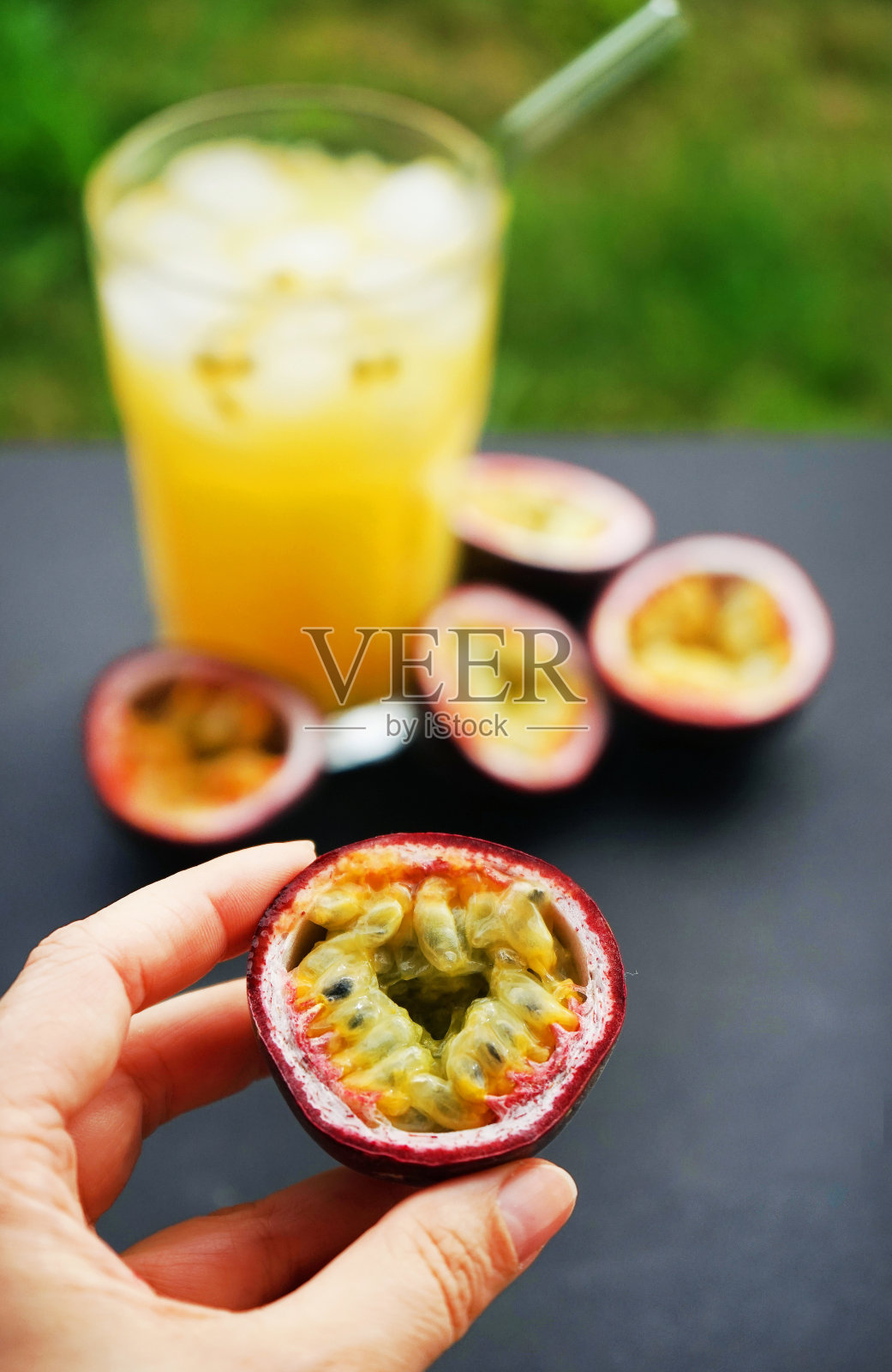 一只手拿着半个百香果，背景是切好的百香果和一杯果汁照片摄影图片