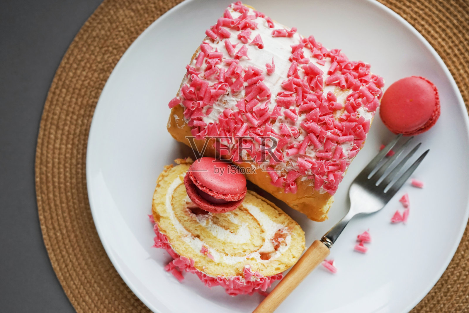 用白色盘子和柳条餐巾盛上奶油、粉色糖屑和覆盆子杏仁饼的海绵卷照片摄影图片