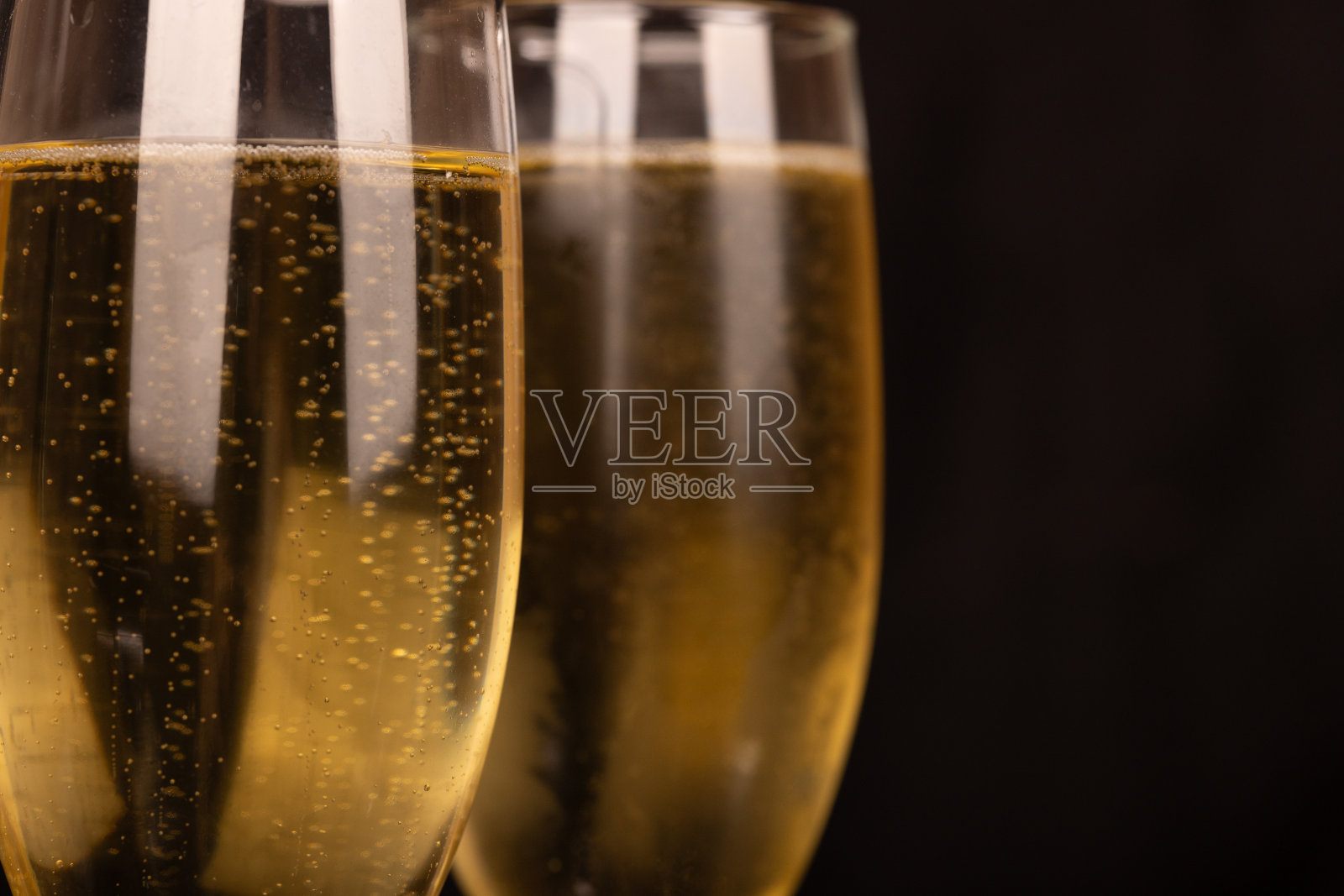 在光滑的黑色背景上，香槟酒杯里装满了气泡饮料。适合圣诞节和派对等节日场合。照片摄影图片