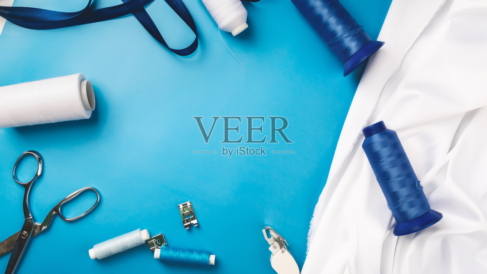 缝纫的概念。女裁缝的办公桌。纺织品，线和剪刀在蓝色背景上顶视图copyspace照片摄影图片