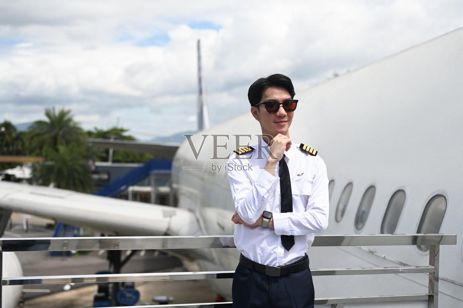 戴着墨镜的男飞行员站在飞机旁边的栏杆上。照片摄影图片