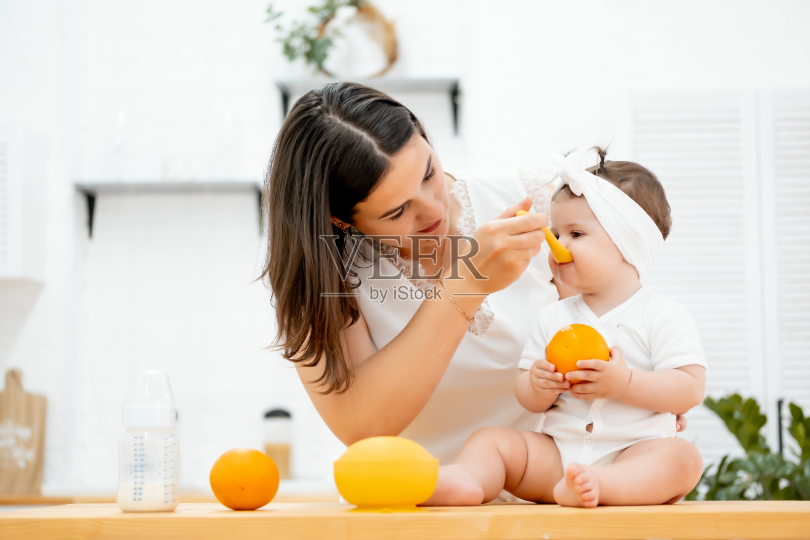妈妈在家里的厨房里用勺子喂宝宝，概念宝宝吃的是水果桔子照片摄影图片