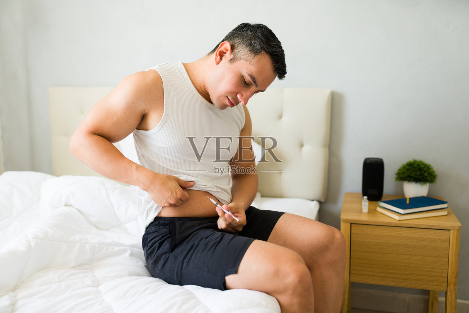 早晨，一个人坐在床上，正在给腹部注射胰岛素照片摄影图片