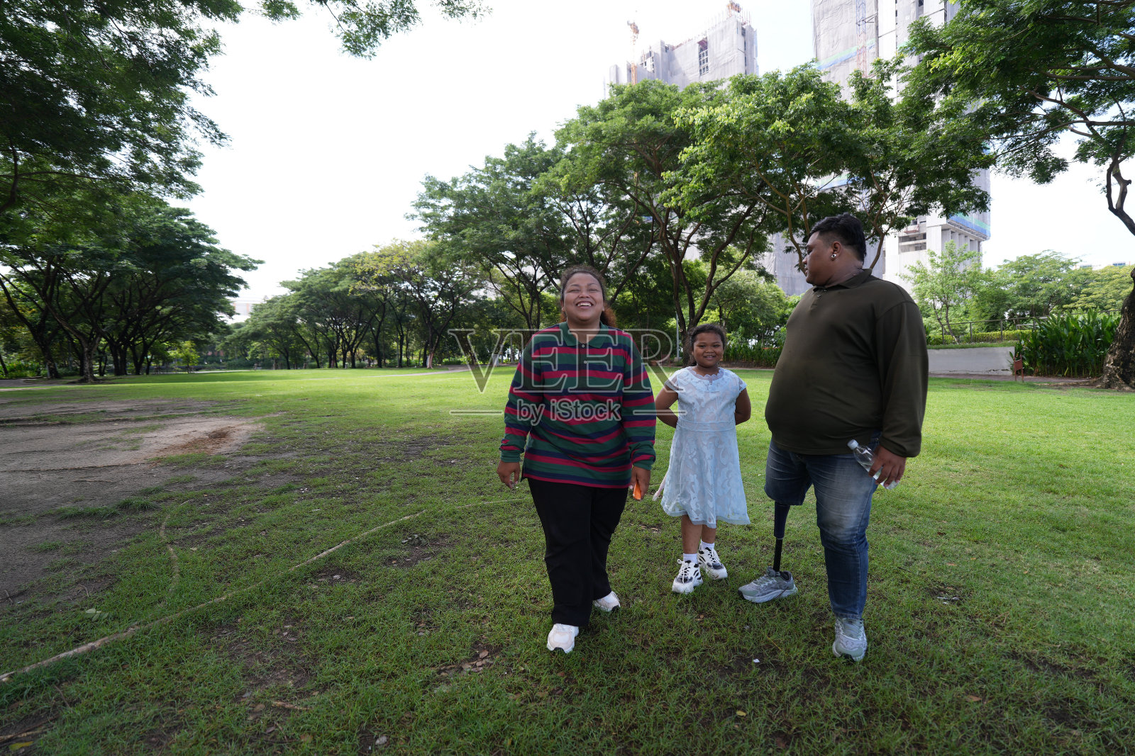 一个又大又胖的亚洲家庭，爸爸、妈妈、女儿在公园里野餐，他们坐着吃零食。他们坐着做作业，互相送花。他们很开心。照片摄影图片