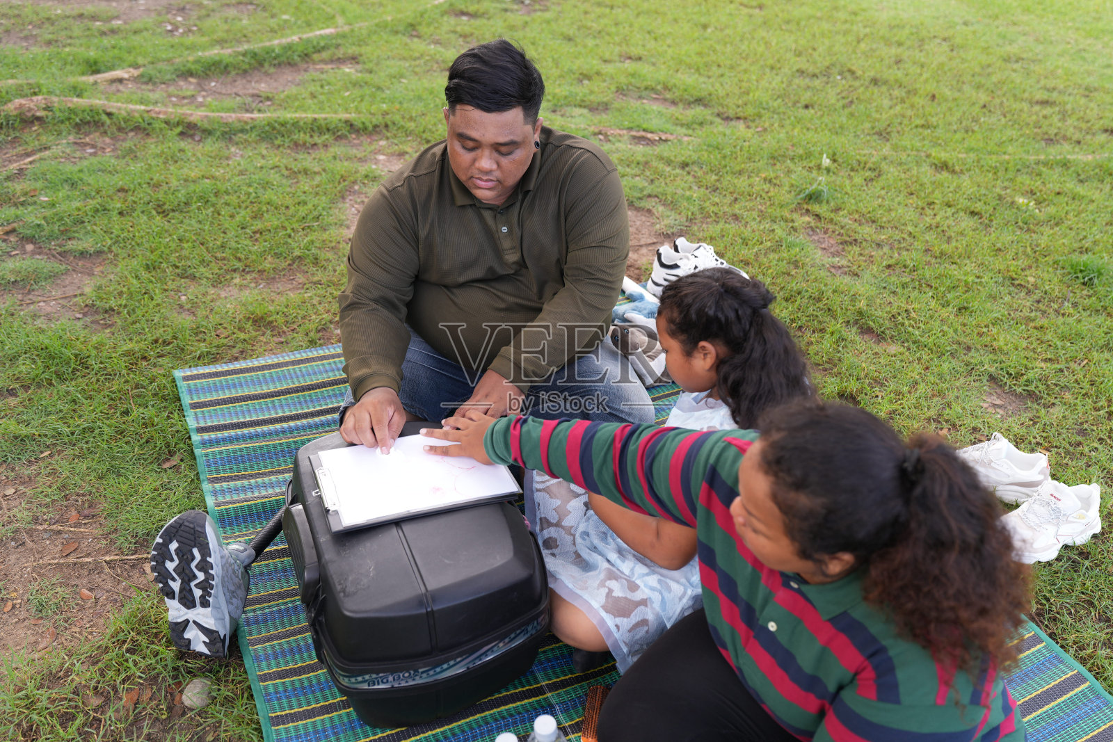 一个又大又胖的亚洲家庭，爸爸、妈妈、女儿在公园里野餐，他们坐着吃零食。他们坐着做作业，互相送花。他们很开心。照片摄影图片