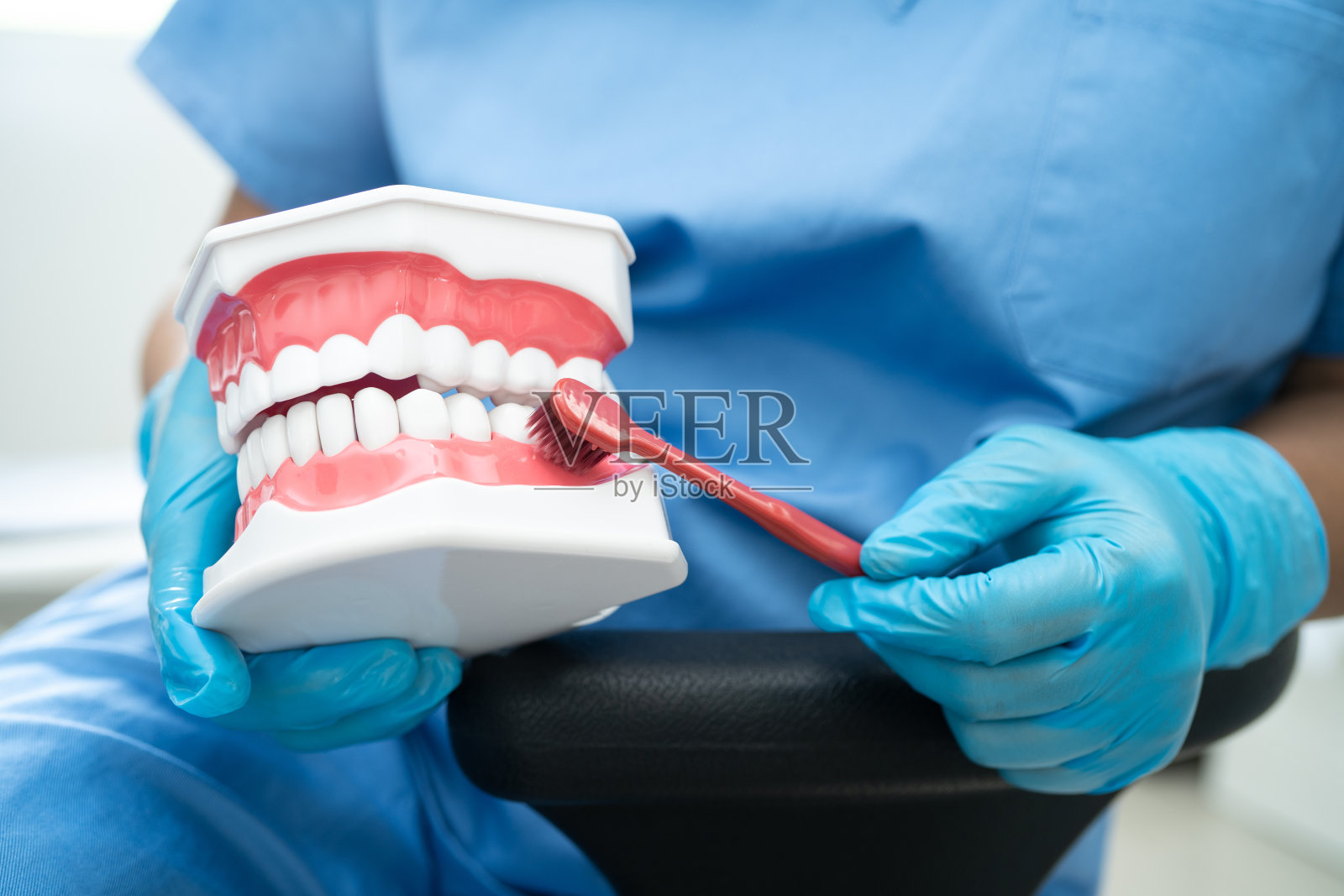 亚洲牙医用牙刷为病人清洁牙齿模型，学习牙科知识。照片摄影图片