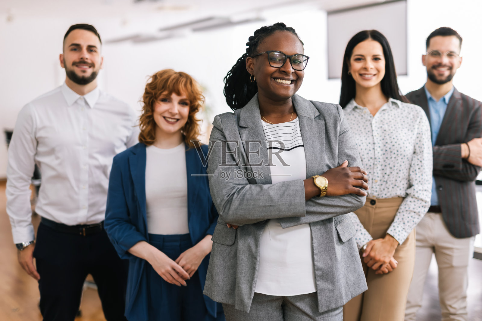 年轻的非裔美国女企业家站在她的同事面前，双臂交叉。照片摄影图片