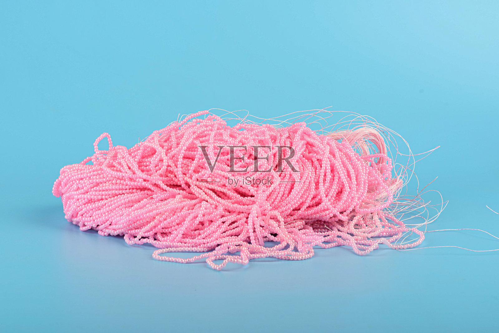 一串粉红色的珠子系在钓鱼线上，放在蓝色的背景上。照片摄影图片