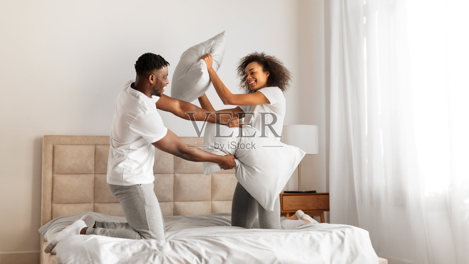 非裔美国夫妇在卧室里玩枕头大战照片摄影图片
