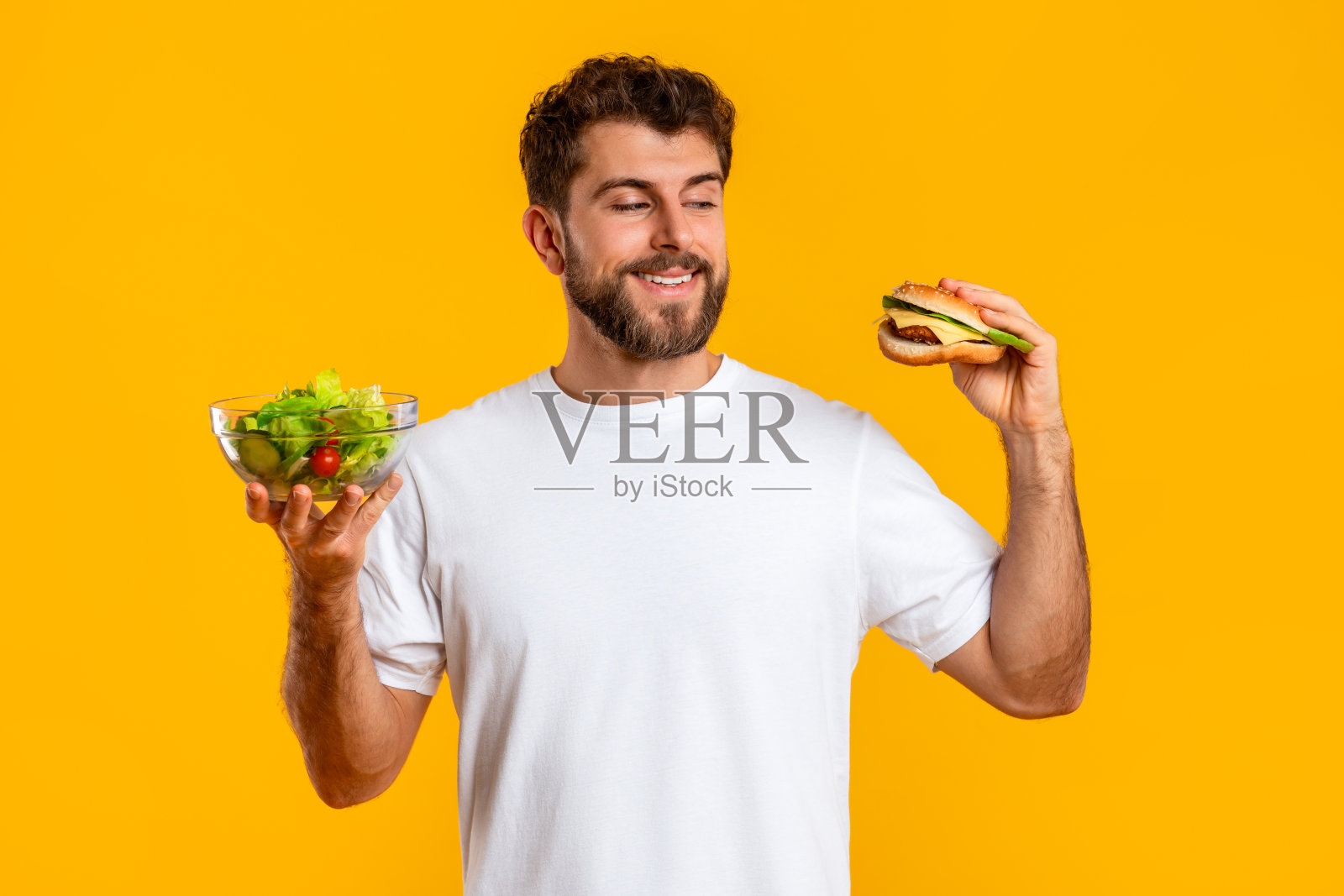 饥饿的年轻人在汉堡和沙拉之间选择，黄色背景照片摄影图片