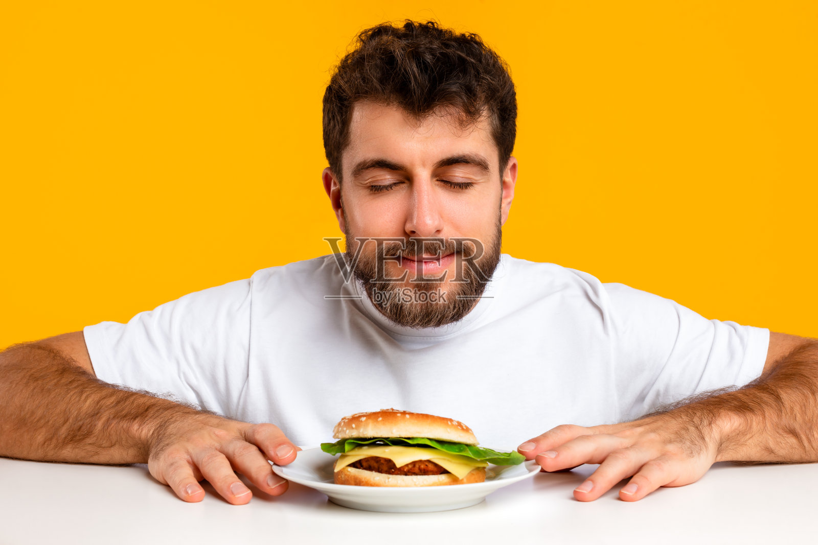 年轻的白人男子闭上眼睛闻着诱人的汉堡，黄色背景照片摄影图片