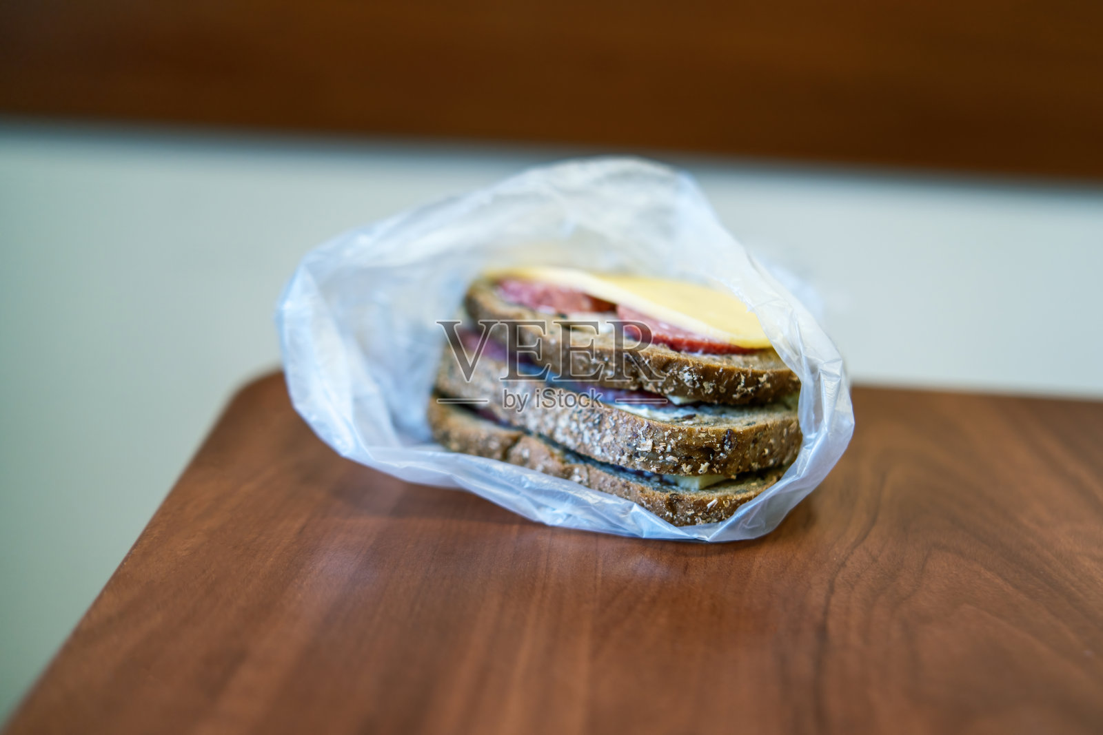 简单而诱人的场景捕捉了黑麦三明治，熏香肠和奶酪，被亲切地包裹在塑料袋里，象征着上班族午休的忙碌照片摄影图片
