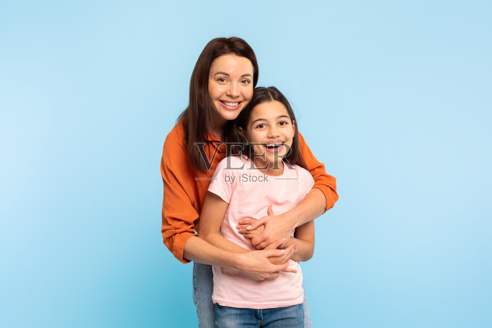爱的妈妈拥抱可爱的青春期前的女儿在蓝色工作室背景照片摄影图片