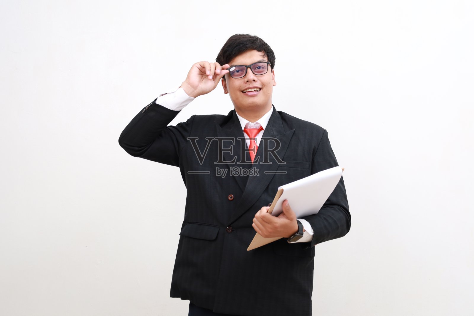 年轻的商人，戴着眼镜的办公室职员经理，拿着写字板，看起来很专业，站在白色的背景下照片摄影图片