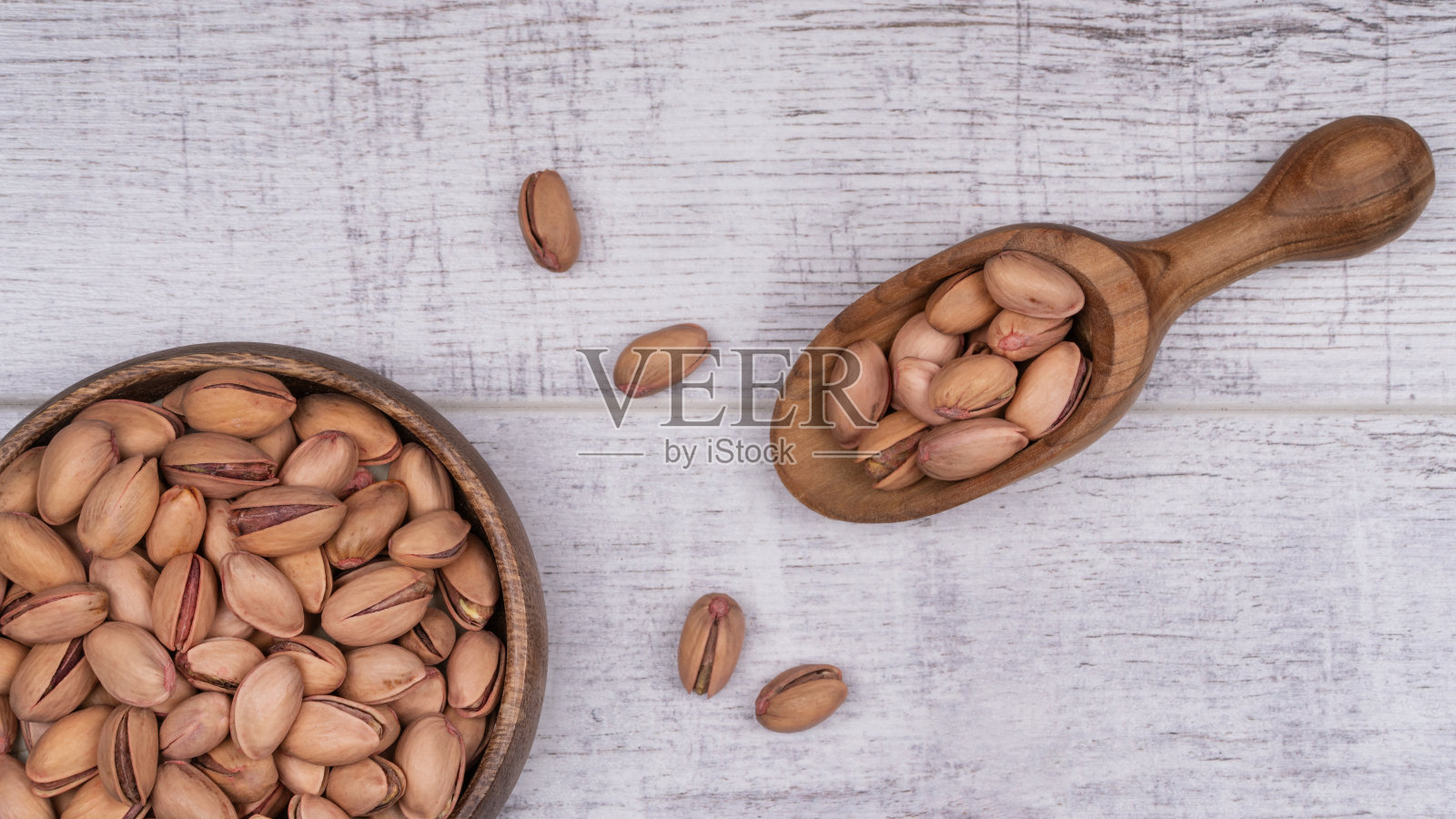 一碗开心果，旁边是一匙开心果木桌。照片摄影图片