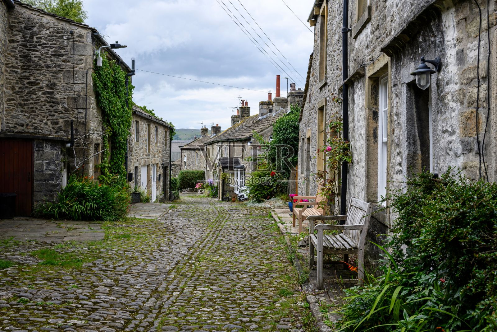 一条古色古香的鹅卵石街道，坐落在一个历史悠久的村庄里，有石头房子和郁郁葱葱的绿色植物照片摄影图片