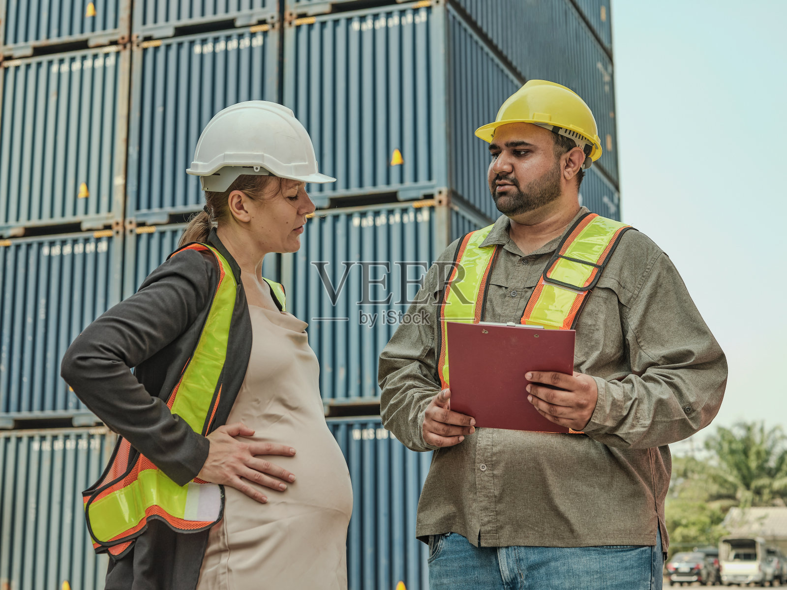 男员工帮助怀孕的女员工或工程师控制集装箱装卸货物。照片摄影图片