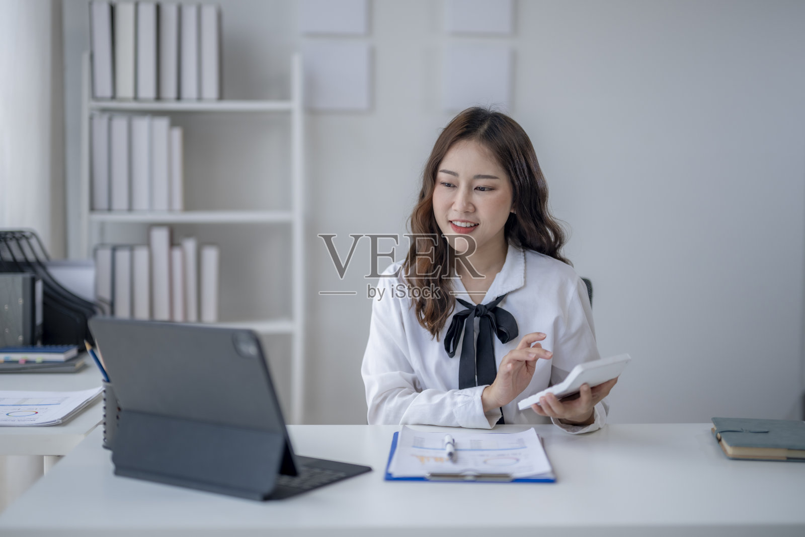 一个女人坐在桌子前，手里拿着笔记本电脑和平板电脑照片摄影图片