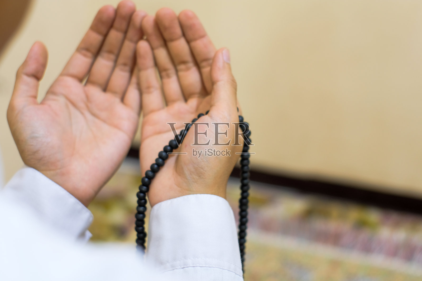 特写后视图穆斯林教徒的手，穿着白色科科衬衫，戴着无边便帽，举起双手虔诚地祈祷，手里拿着伊斯兰念珠。照片摄影图片