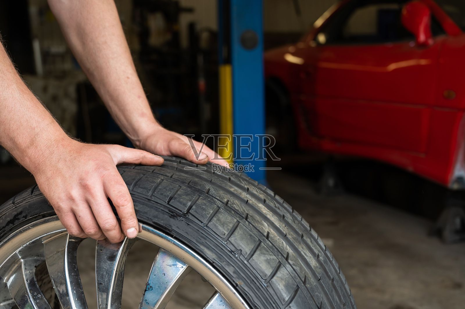 汽车修理工拿着汽车的轮子。根据季节更换汽车轮胎照片摄影图片