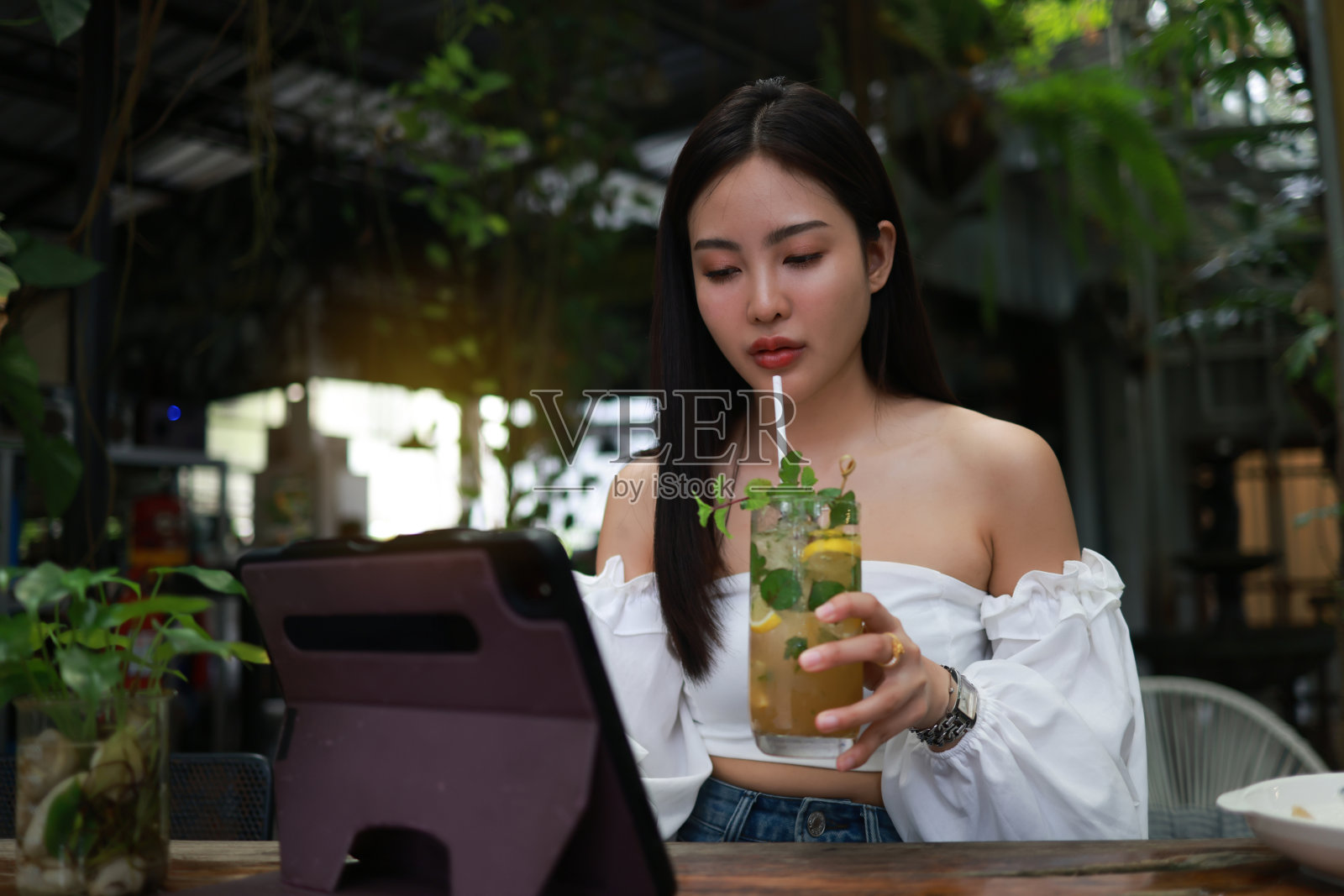 一个年轻女子的自信形象，一边喝着冷饮，一边用她的数码平板电脑放松。照片摄影图片