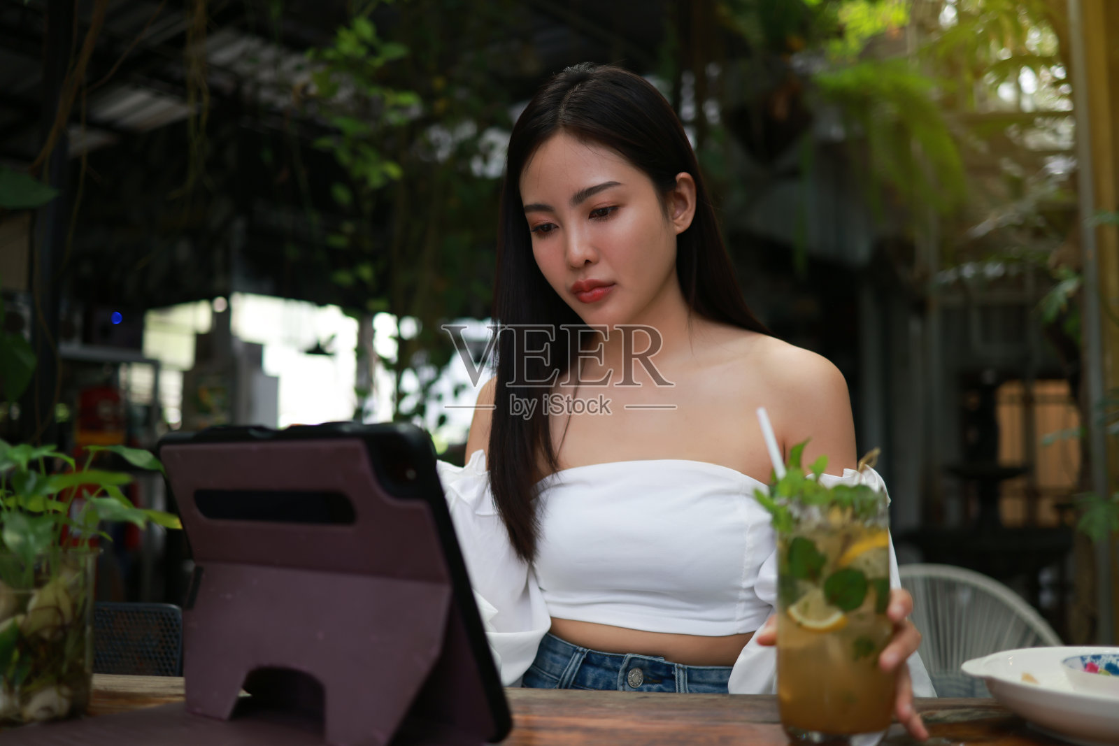 一个年轻女子的自信形象，一边喝着冷饮，一边用她的数码平板电脑放松。照片摄影图片