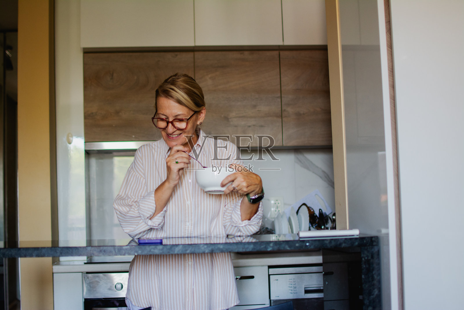 成熟的金发女人戴着眼镜，在更年期吃健康均衡的早餐照片摄影图片